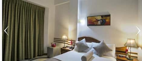 A hotel room with a large bed, two bedside tables, a painting on the wall, and a green curtain.