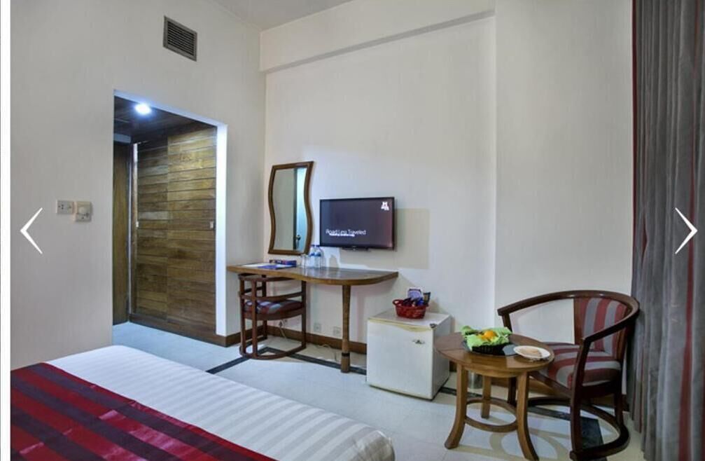 A hotel room with a bed, a desk with a chair, a television, a small refrigerator, and a window with curtains.