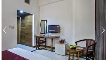A hotel room with a bed, a desk with a chair, a television, a small refrigerator, and a window with curtains.