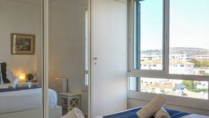 A hotel room with a bed, a window with a city view, a bedside table, and a wall-mounted picture. - Balmins White by Hello Homes Sitges (Sitges)