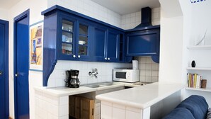 A compact kitchen with white countertops, blue cabinets, a microwave, a coffee maker, and a small wooden cabinet. - Barco Attic by Hello Homes Sitges (Sitges)