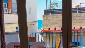 A balcony with a table and chairs, a view of the sea, and a building with a red roof. - Barco Attic by Hello Homes Sitges (Sitges)