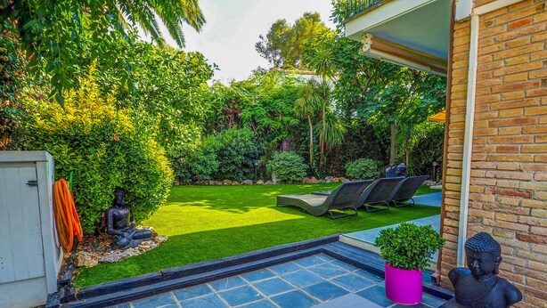 Un jardin bien entretenu, avec une pelouse, une petite piscine et deux chaises longues.