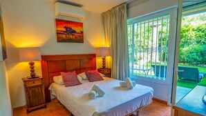 Une chambre d’hôtel avec un grand lit, deux tables de chevet, une commode, un tableau au mur et une vue sur le jardin par la fenêtre.