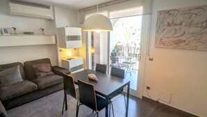 Una sala de estar moderna con un sofá, una mesa de comedor y sillas. Hay un ventanal con vistas al exterior.