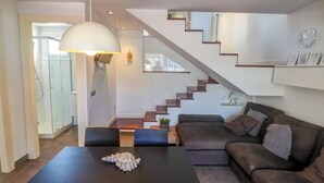 Una sala de estar moderna con una mesa de comedor de madera oscura, un sofá grande y una escalera de diseño minimalista.