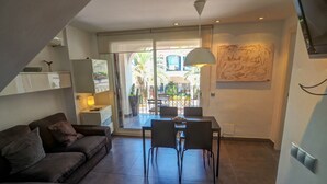 Una sala de estar moderna con un sofá, una mesa de comedor con sillas, una lámpara colgante y vistas al balcón exterior.