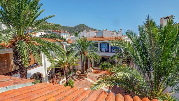 Una zona residencial con tejados de tejas color terracota, palmeras y edificios blancos con detalles azules.