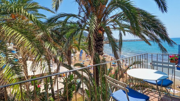 A balcony with a view of a beach, palm trees, and a table with chairs. - Port Alegre Attic by Hello Homes Sitges (Sitges)