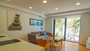 A modern living room with a glass-top dining table, orange chairs, a sofa, and a large window with a view of palm trees. - Port Alegre Attic by Hello Homes Sitges (Sitges)