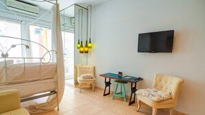Hotellihuone, jossa on sänky, kaksi tuolia, pieni pöytä, televisio ja ikkuna, jossa on verhot.