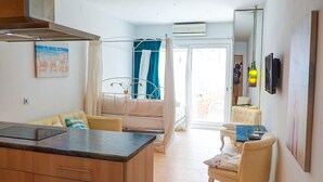 Moderni hotellihuone, jossa on keittotila, ruokapöytä, sohva ja suuri ikkuna.