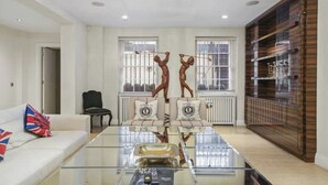 A modern living room with a glass coffee table, a sofa with a Union Jack pillow, and two wooden sculptures. - Magnificent House in Knightsbridge (London)