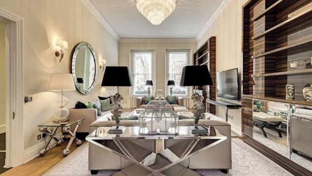 A spacious living room with a modern chandelier, a large mirror, and a television on a wooden shelf. - Magnificent House in Knightsbridge (London)