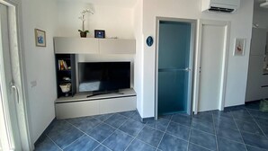 A modern living room with a flat-screen TV, a small plant, and a bookshelf. - La Miravè holiday home located in Praiano, jewel of the Amalfi Coast. (Praiano)