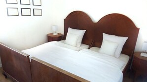 Un lit double avec une tête de lit en bois, deux tables de chevet et un couvre-lit blanc.
