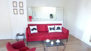Un salon avec un canapé rouge, un fauteuil rouge et une table basse sur laquelle se trouvent des tasses et une théière.