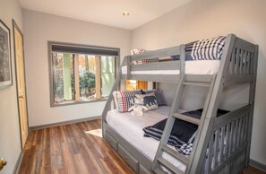 Quarto com beliche, janela, piso de madeira e porta.