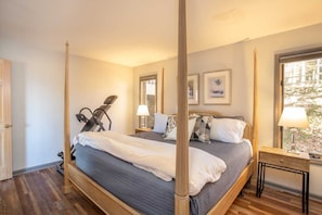 A four-poster bed with a grey bedspread, a wooden floor, a standing exercise machine, and a window with a view of trees. - Expansive Home on Beech Mountain (Beech Mountain)