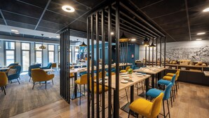 Un comedor moderno con mesas altas, sillas, un separador de vidrio e iluminación colgante.