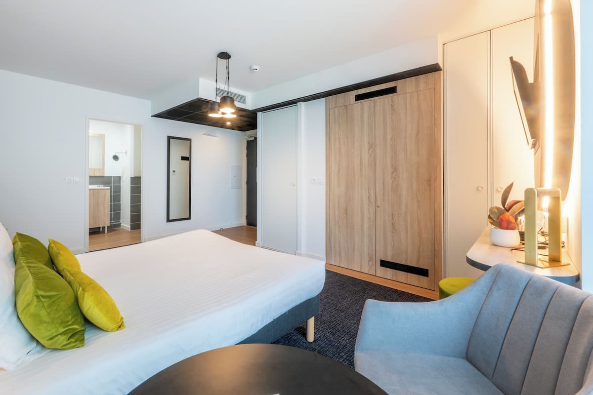 A modern hotel room with a large bed, a sofa, a small table, and a wardrobe.