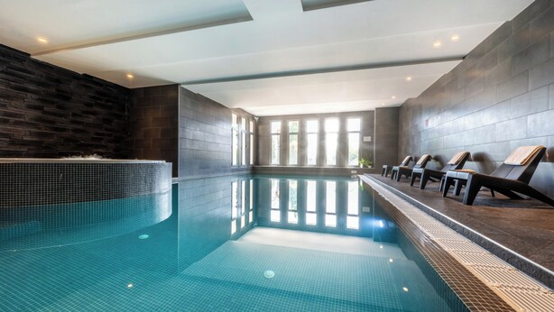 Una piscina interior con paredes y techo azulejados, un banco largo a lo largo de un lado, y ventanas amplias que dejan entrar luz natural.