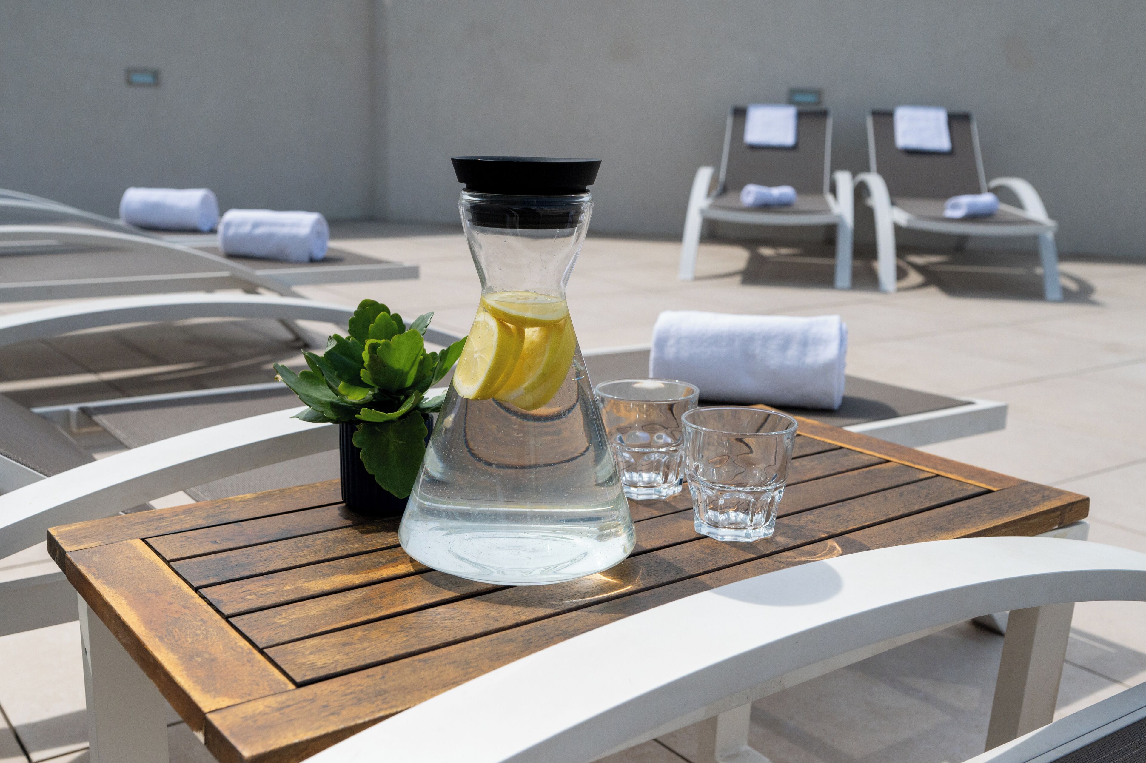 Une table en bois sur laquelle se trouvent une bouteille en verre transparent contenant une boisson, une petite plante en pot et deux verres.