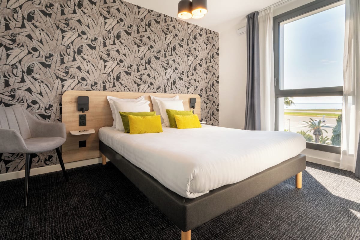 A hotel room with a large bed, a nightstand, a chair, and a view of the ocean.