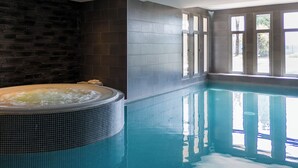Una piscina con hidromasaje, paredes con azulejos y ventanas amplias.