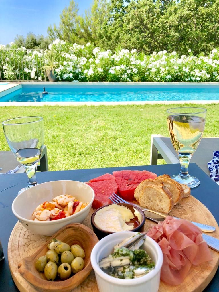 A table set outdoors with a pool view, featuring a variety of food including olives, cheese, and bread.