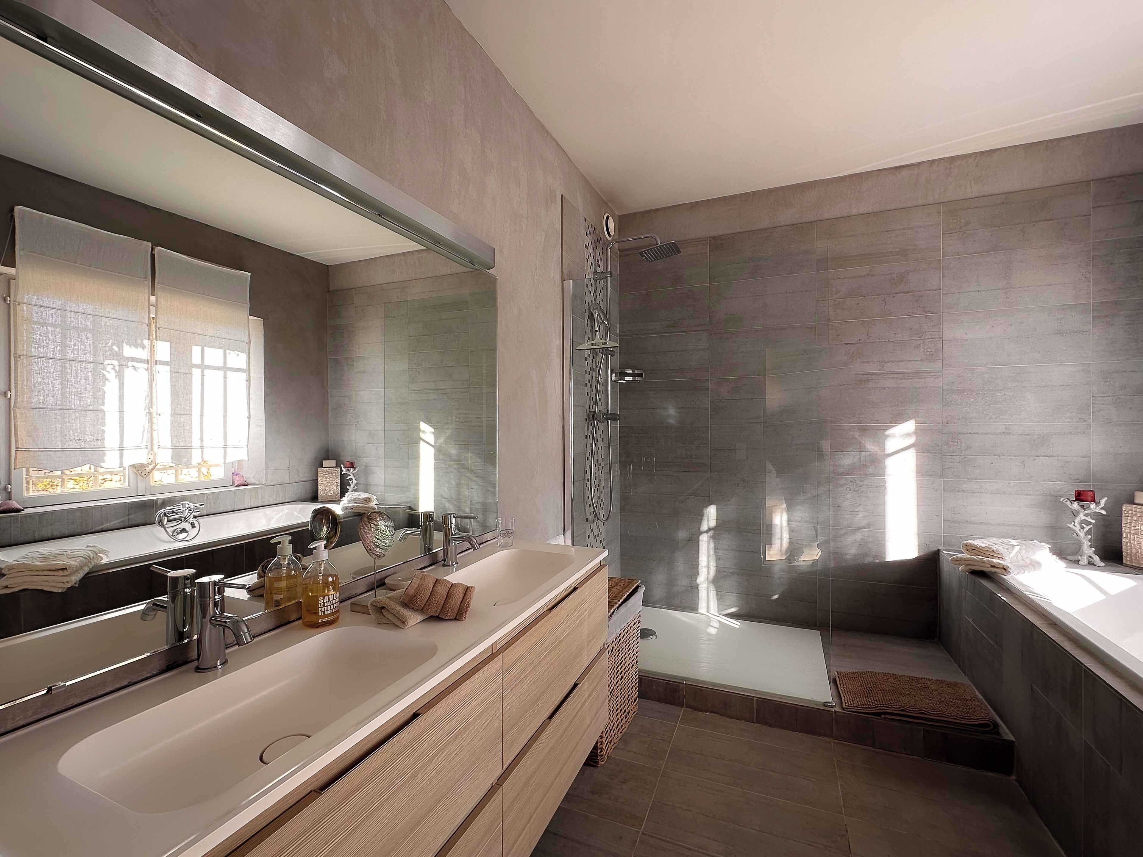A modern bathroom with a large mirror, dual sinks, a glass shower enclosure, and a wooden vanity.