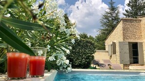 En swimmingpool med en byggnad i sten som syns i bakgrunden, omgiven av grönska och vita blommor.