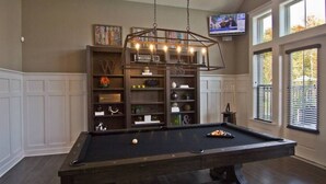 Een pooltafel met een hanglamp erboven, omringd door planken met diverse decoratieve objecten.