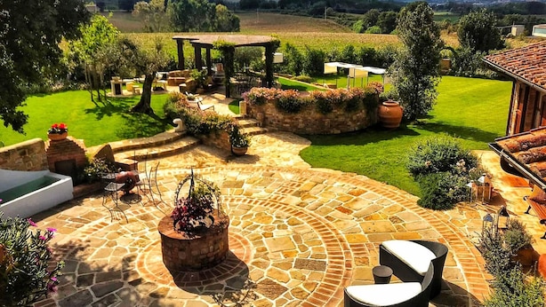Eine Steinterrasse mit Gartenmöbeln, einem Whirlpool und einem Pergola mit Kletterpflanzen.