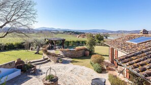 A courtyard with stone flooring, a pergola, outdoor seating, and a view of distant hills. - Casale Bella Vita 8 4 (Citta della Pieve)