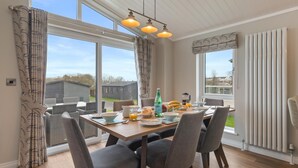 A dining area with a wooden table, grey upholstered chairs, and a view of the outside.