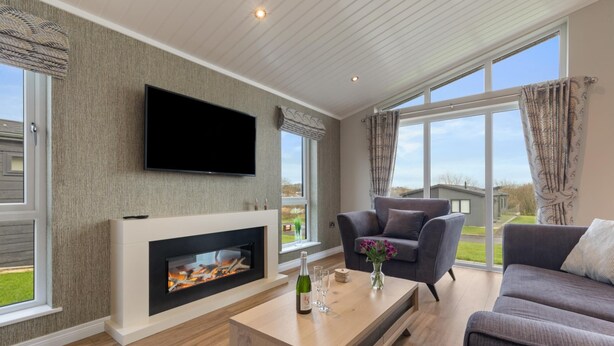 A modern living room with a fireplace, a flat-screen TV, and a large window offering a view of the outdoors.