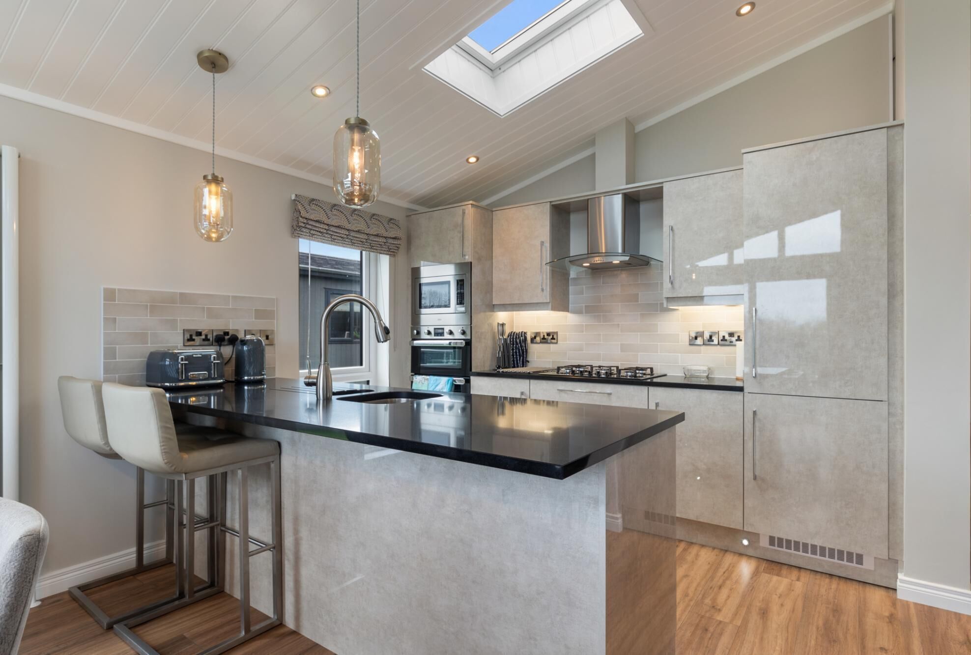 A modern kitchen with a central island, stainless steel appliances, and a skylight.