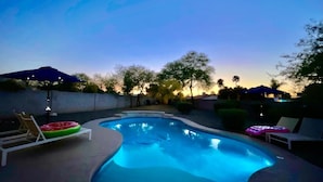 A swimming pool with lounge chairs and umbrellas, surrounded by trees and a sunset in the background. - The Scott With Heated Pool by Homeslice Stays (Scottsdale)