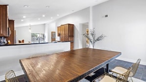 A modern kitchen with wooden cabinets, a large island, and a dining area with a wooden table and chairs. - The Scott With Heated Pool by Homeslice Stays (Scottsdale)
