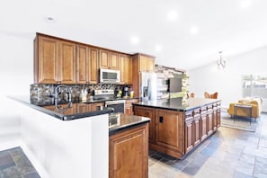 A modern kitchen with wooden cabinets, a central island, and a dining area with a yellow sofa. - The Scott With Heated Pool by Homeslice Stays (Scottsdale)