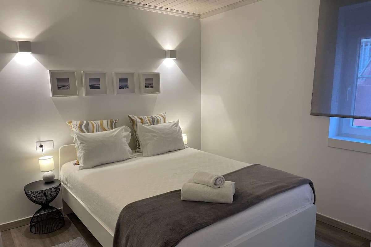 A neatly arranged bedroom with a bed, bedside lamps, a small round table, and a window with a view.
