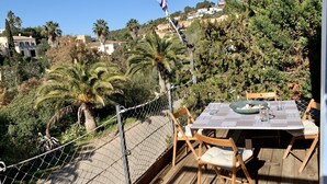 Una terraza de madera con una mesa y sillas, con vista a una zona residencial con casas y palmeras.