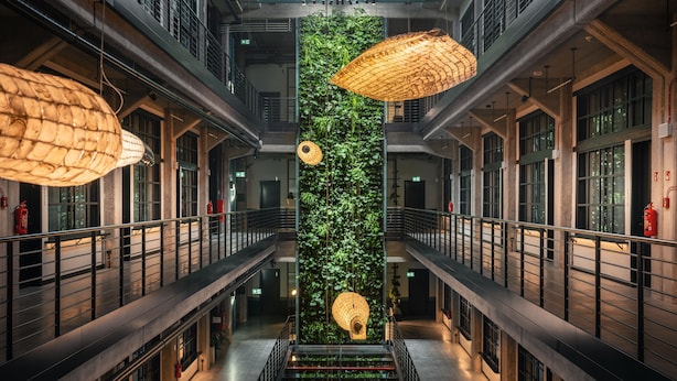Um interior com vários níveis, um jardim vertical central, grades de metal e luminárias pendentes.