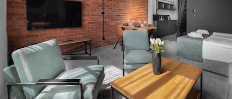 A modern living room with a brick wall, a flat-screen TV, a wooden coffee table, and a sofa.
