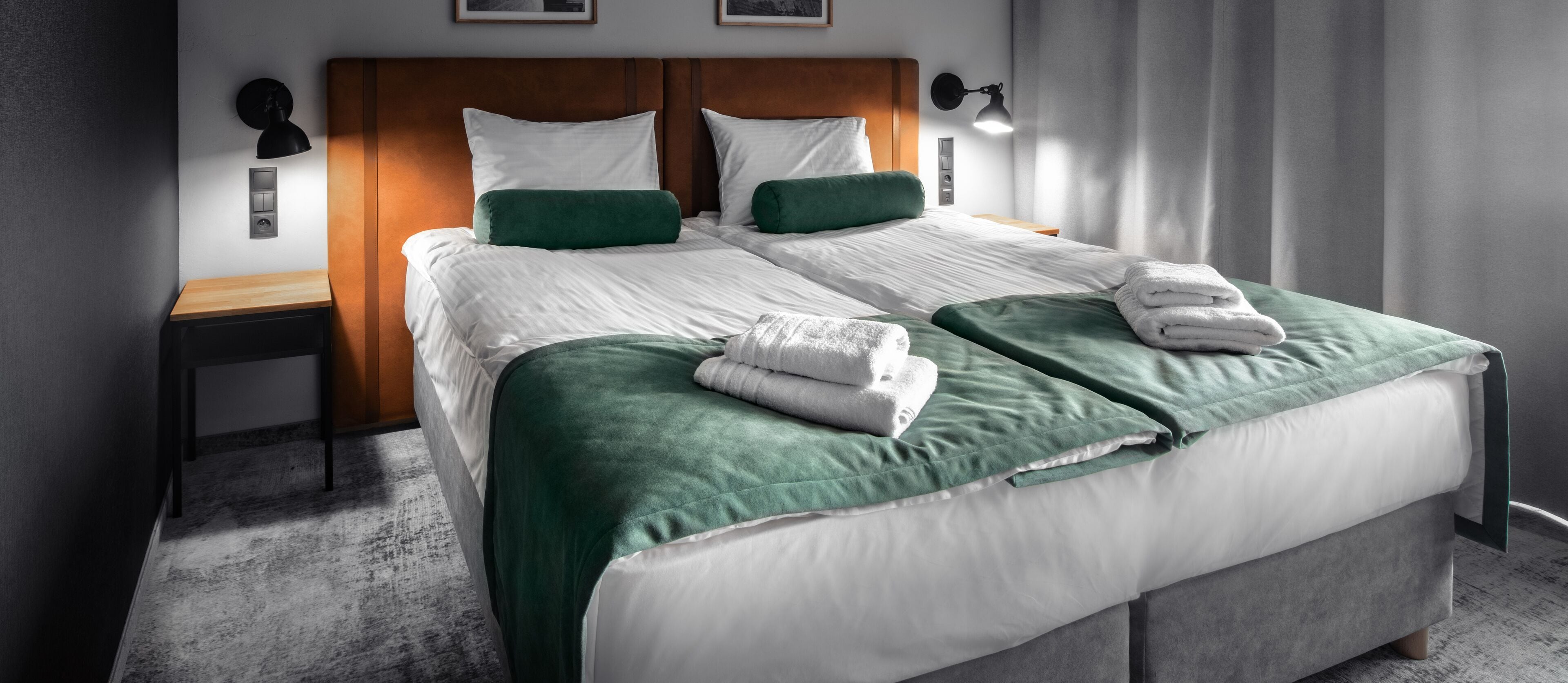 Ein ordentlich bezogenes Bett mit weißer und grüner Bettwäsche, ein hölzernes Kopfende und zwei Nachttischlampen.