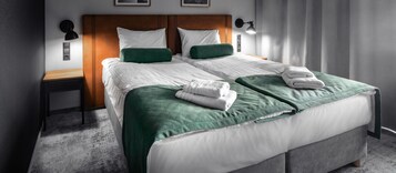 Una cama bien tendida con ropa de cama blanca y verde, un cabecero de madera y dos lámparas de noche.