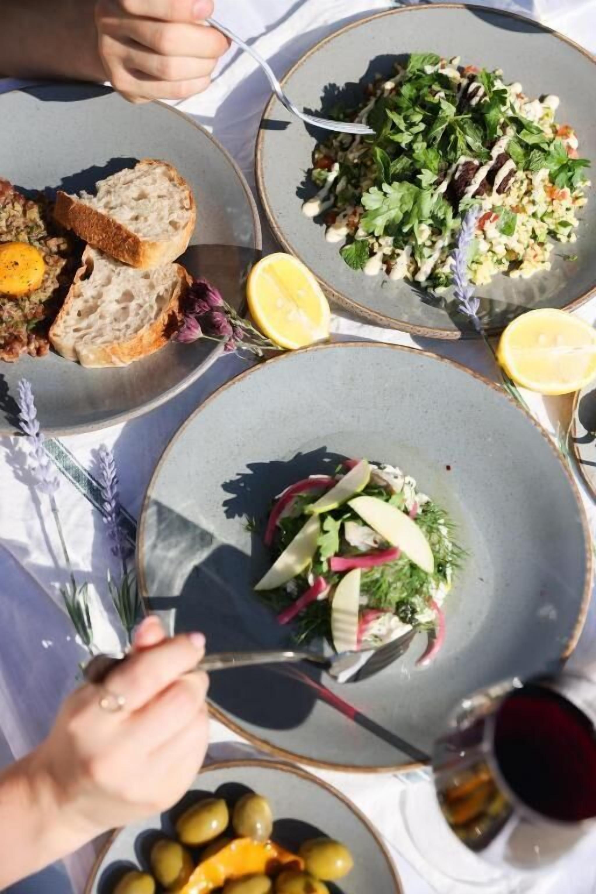 A table with plates of food, including bread, salad, and olives, and a glass of red wine.