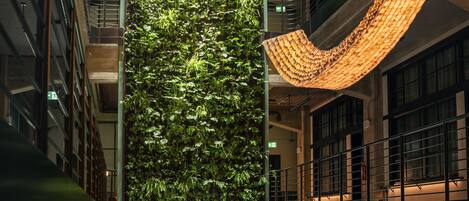A modern building interior with a vertical garden, a curved light fixture, and a glass floor.