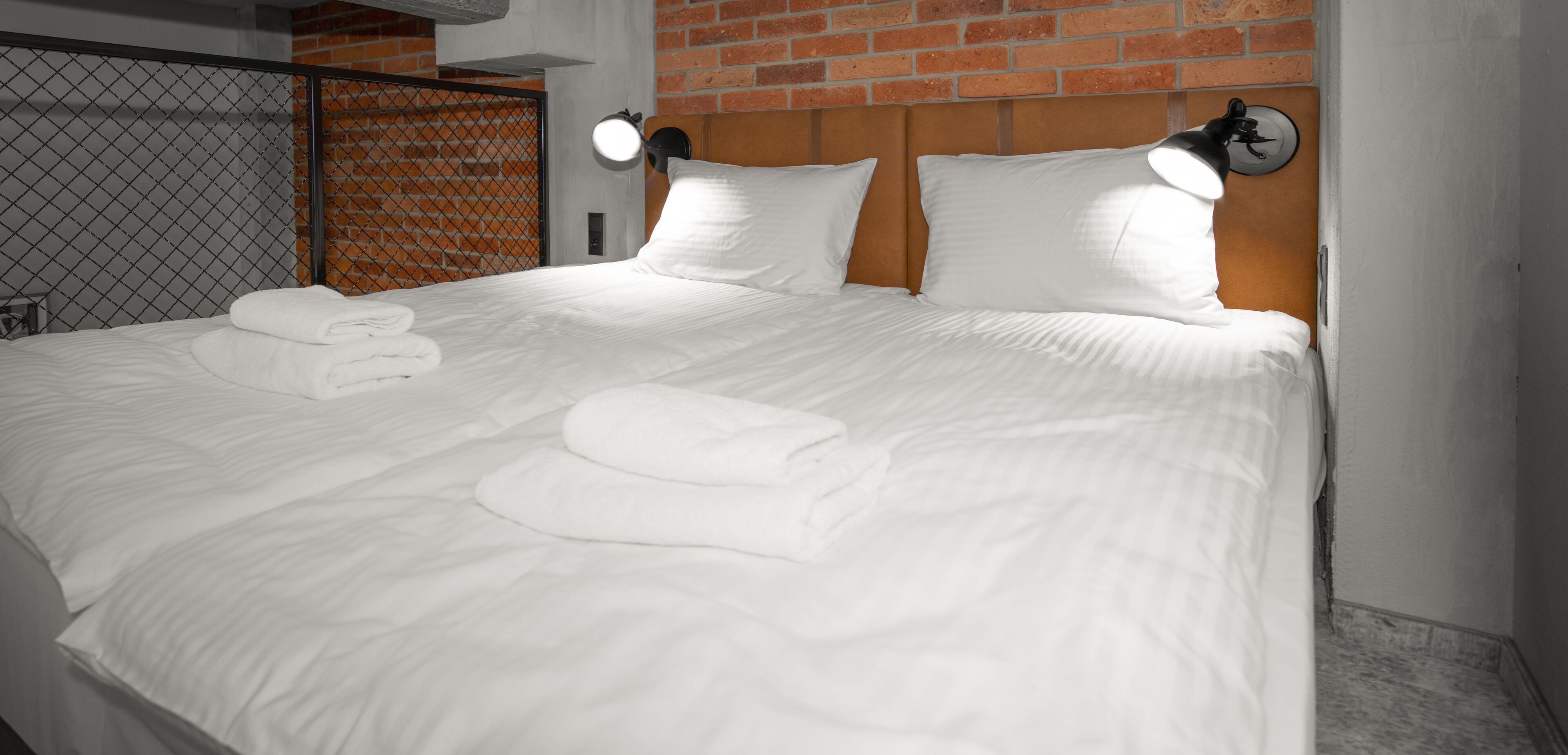 A neatly made bed with white linens and two pillows, a headboard with a brick pattern, and two wall-mounted reading lamps.
